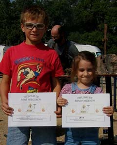 A young boy and a small girl hold their "diplomas" for completeing the "mini forgeron" course.