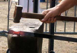 A hot piece of steel is being shaped by hand with a hammer on a large anvil.