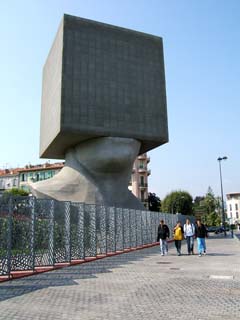giant sculpture is shoulders and neck of a man with building sized cube on top.