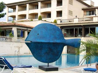 Large abstract fish painted blue in front of the main pool with the main building and conference center in back.