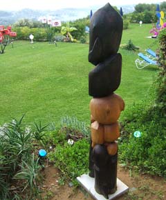 An abstract totem of polished wood of two colors.  More sculptures in the background.