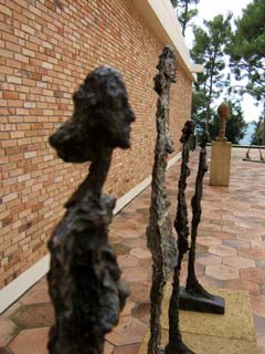 Four highly textured figures of women stand side-by-side in a row.  A bust of his brother Diego, and walking man in the background.