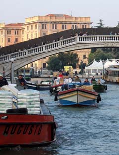 A crowd of supply boats enter the city along the Grand Canal.  In the background is a foot bridge.  In the middle of the frame is a yellow square with the image of the "Mona Lisa".
