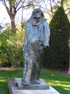 A monumnetal sculpture of a man walking while wrapped dramatically in a large coat.