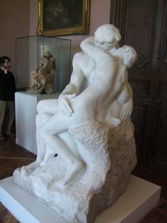 A marble version of the famous sculpture "The Kiss" with an earlier terra cotta version in the background.