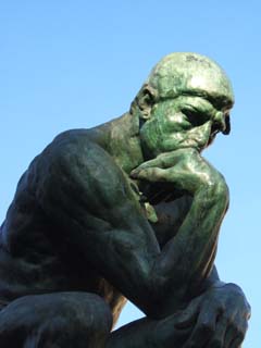 A monumental bronze version of the familiar Rodin sculpture known in English as "The Thinker".  The morning sun is just reaching the figures head.