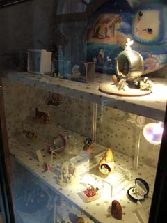 a glass display case contains a number of small creches each of which is a slef contained object.  in the upper right is a steel ball (used for the game Petank) that has been cut in half and surmounted with a cross.  The hollow inside the ball has been filled with a nativity scene.