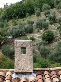 A short chimney on a tile roof frames a hillside of terraced gardes nin the background.