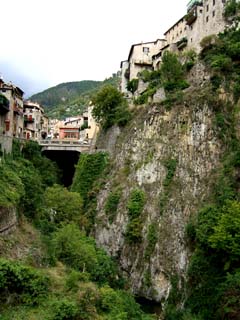 Buildings perched high on the rock on either side of a deep ravine.  A bridge is visible midway up the hight of the ravine.  Building span the ravine in places further back into town.