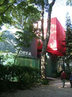 Nestled in the trees is a building made up of a cylinder and a couple of cubes mostly painted in a subdued green-gray but the top is like a bright red oriental lantern.