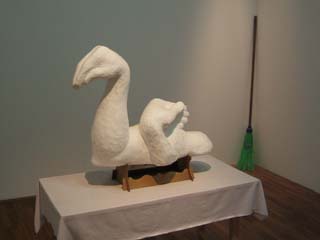 A sculpted piece of styrofoam is carved to look like two realistic human arms that are positioned to create the form of a swan: on arm is bent upward to form a neck with the hand becoming the head and beak while the other arm crosses the bicept of the first so that the hand and fingers look like the wing and feathers of the swan.  Very nicely done.