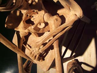 close up of the skeletons lap and right arm which is holding a knife--all carved out of one large laminated block of light colored wood.  The level of acuracy is excrutiating.  Visible in the photo are indications of the direction of the grain in the original block.