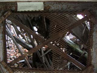 A colapsed building is visible through a small rusted opening.  Heavy beams, broken roof tiles and other debris lay scattered.  The overall composition is not unpleasant.