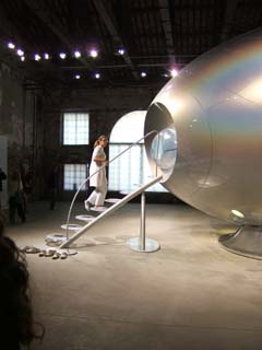 A woman in a lab coat ascends a futuristic staircase.  Four pairs of white clogs wait at the ground.