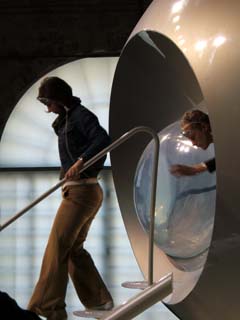 two people with electrodes attached to their foreheads are exiting the futuristic looking exhibit.