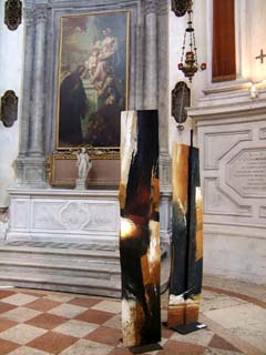 two earth tone abstracts painted onto two rectangular slabs of steel contrast with the elaborately decorated walls of a Venitian building.