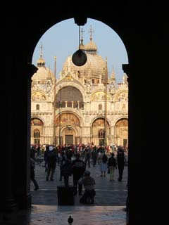 An archway frames the Piazza San Marco, one of the most recognizable sites in Venice.  At the base of the picture is a pigeon.  Tourists in background are snapping photos for relatives and friends who have been left behind.