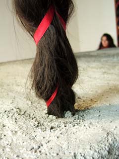 Close up view of one of the four braids stuck in concrete.  In the background is the blurred image of a young woman with laong hair of the same color.