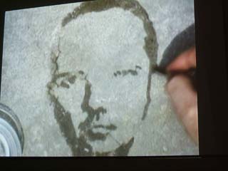 a partially evaporated image of a man's face and the artist's hand.