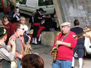 A saxaphone player leans back into a note accompanied by another sax, a trumpet, and a picalo.  In the background other performers relax.