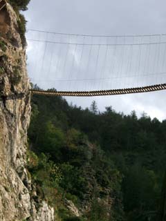 A foot bridge is suspended high above and termintates into a steep cliff.