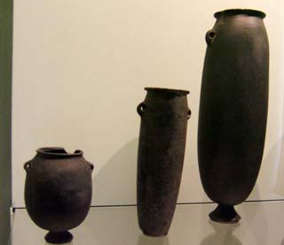 Three dark gray vessels made out of basalt rock appear to be perfectly roound as if turned on a potters wheel except for small protruding handles.