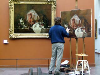 A young man stnads in front of an easil and glances at the original oil painting that he is copying.  This time honored way of learning apparently continues but it is the first time I have ever seen it.