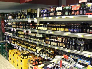 A grocery store display shelf full of beer and more stacked on the floor.