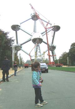 A young girl looks wearily at an oncoming taxi as her father uses her as a prop to give scale to the giant Atomium sculpture in the background.