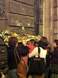 A bronze sculpture of a saint has been polished bright yellow by the hands of inumerable travelers.