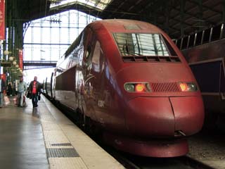 A red colored streamlined high-speed train waits in the station.