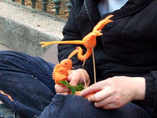 An artist's hands holding a crane and two goldfish carved from carrots.