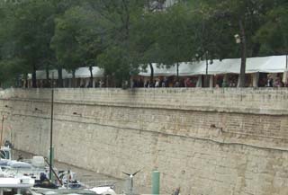 view of the tall stone walls that bank the Seine river as it passes through Paris.  In the foreground are travel barges (sort of house boats but much fancier).  Just behind the top of the wall is a row of tents that made up the Art Fair.