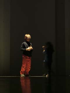 a young boy and a young girl (barely visible as a shadow) play in a pool of light.