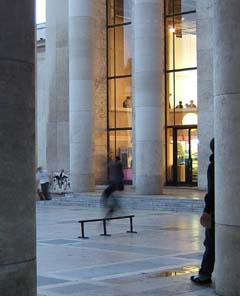 The blurred image of a skater sliding across a steel rail in the middle of marble terrace surrounded by marle columns.