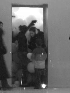 Fuzzy B&W image of a woman exiting a room full of balloons while the attendant attempts to keep them from coming out the door.